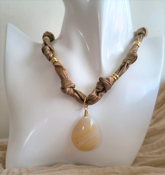 Collier Eloha noué à la main en tissu ocre satiné avec pendentif d’agate rayée naturelle. Bijou artisanal fait main, doux et chaleureux.