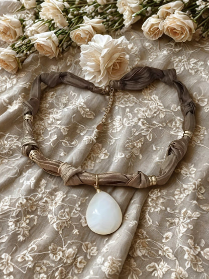 Collier Eloha noué à la main en tissu ocre satiné avec pendentif d’agate rayée naturelle. Bijou artisanal fait main, doux et chaleureux.